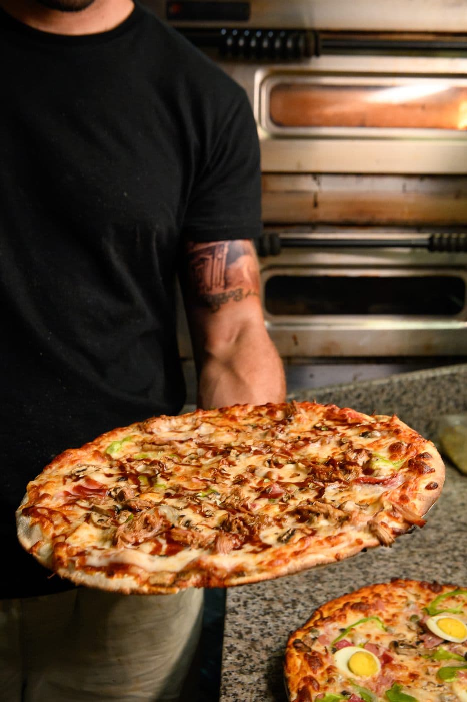A chef carrying a freshly baked pizza past the oven