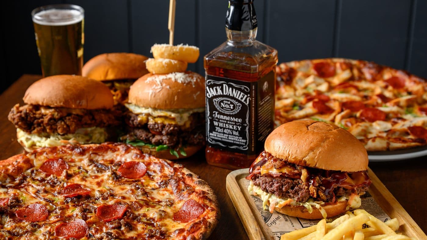 A table laid with burgers, pizza and drinks