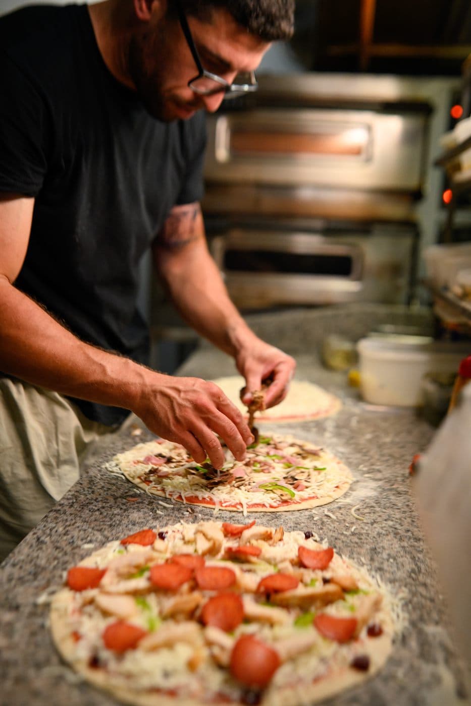 A chef topping a pizza base by hand